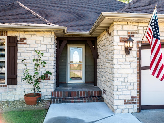 view of exterior entry with stone siding and roof with shingles