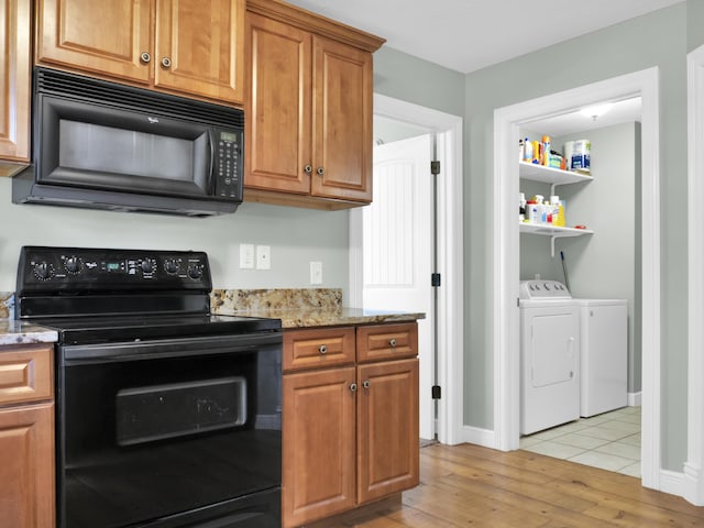 kitchen featuring brown cabinetry, light wood-style floors, light stone countertops, black appliances, and separate washer and dryer