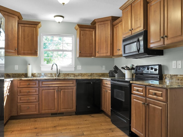 kitchen with brown cabinetry, a sink, light wood-style flooring, and black appliances