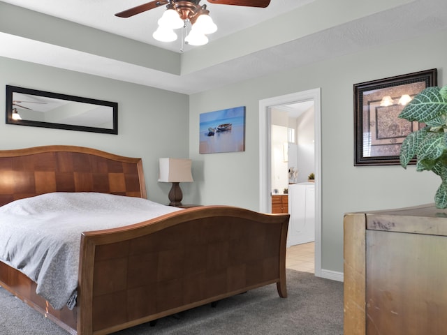 carpeted bedroom featuring ceiling fan, a tray ceiling, ensuite bath, and baseboards