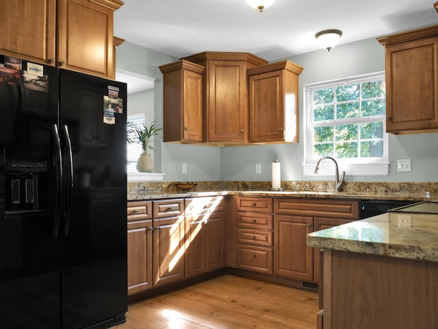 kitchen featuring a sink, light wood-style floors, black fridge, brown cabinets, and light stone countertops