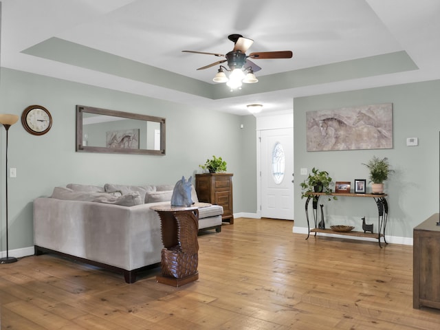 living room featuring light wood finished floors, baseboards, and a tray ceiling