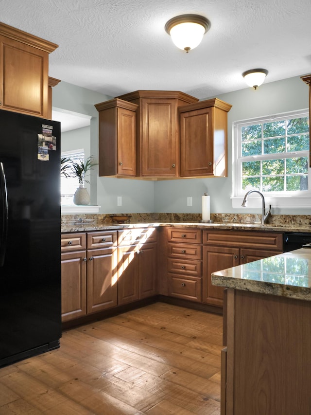 kitchen featuring brown cabinetry, a sink, black appliances, and hardwood / wood-style flooring