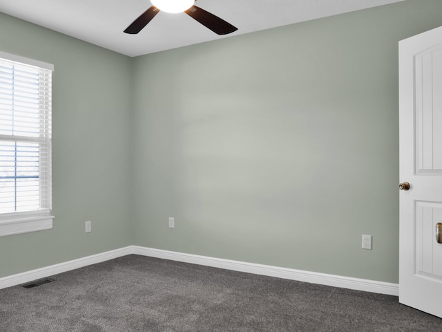 unfurnished room featuring a healthy amount of sunlight, visible vents, dark carpet, and baseboards