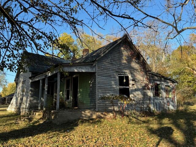 view of side of home with covered porch, a lawn, and a chimney