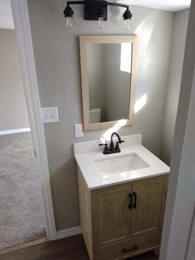 half bathroom with baseboards, a textured wall, vanity, and toilet