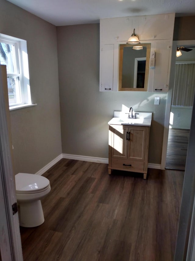 half bathroom with baseboards, toilet, ceiling fan, wood finished floors, and vanity