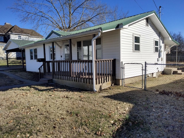 ranch-style home featuring covered porch, a gate, fence, and metal roof