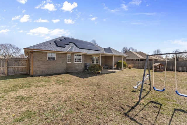 rear view of house featuring a playground, a yard, a fenced backyard, and brick siding