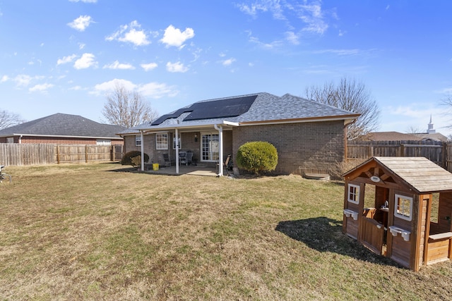 back of property featuring brick siding, a lawn, a fenced backyard, and roof mounted solar panels