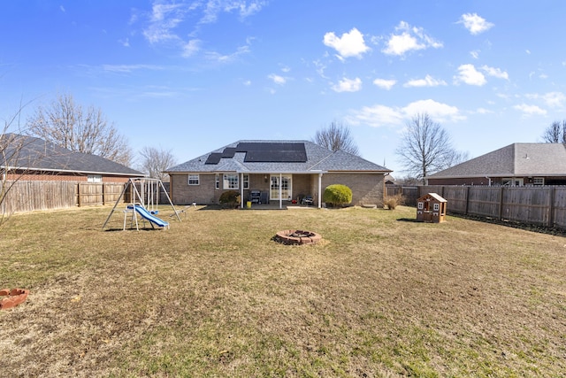 back of house with a fire pit, a playground, a fenced backyard, and roof mounted solar panels