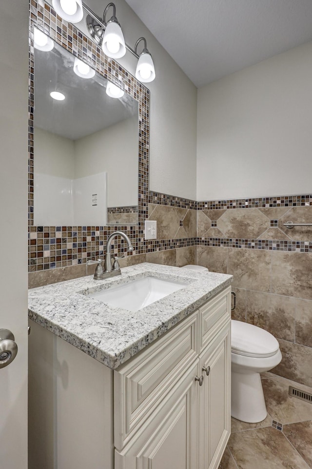 bathroom featuring tile walls, visible vents, toilet, wainscoting, and vanity