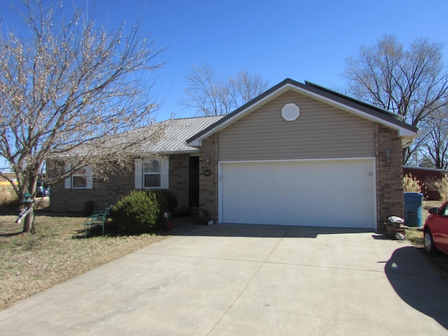 ranch-style home with a garage, concrete driveway, brick siding, and metal roof