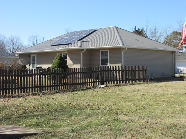 view of home's exterior with a yard, metal roof, a fenced front yard, and solar panels