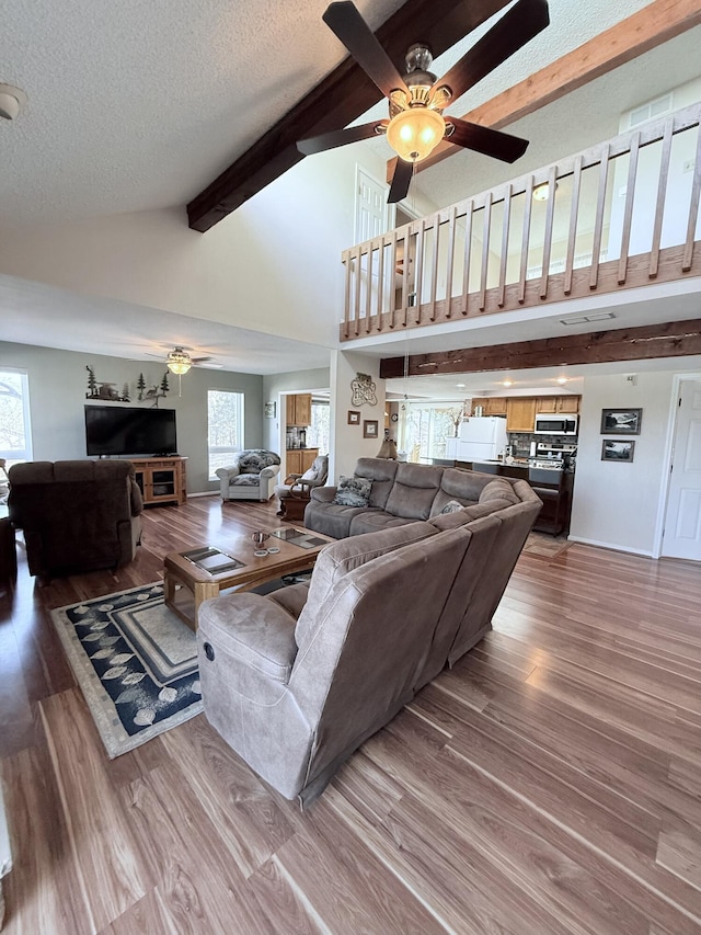 living area with a healthy amount of sunlight, a textured ceiling, beamed ceiling, and wood finished floors