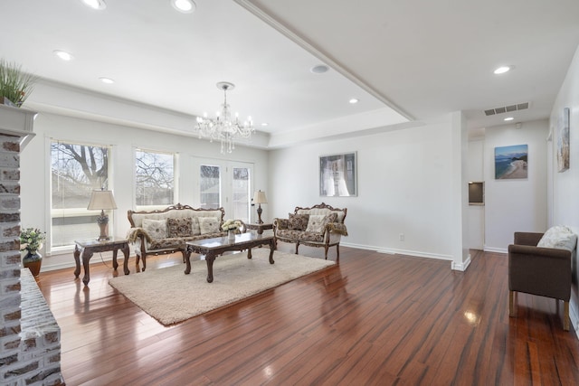 living area with a wealth of natural light, a tray ceiling, hardwood / wood-style flooring, and visible vents