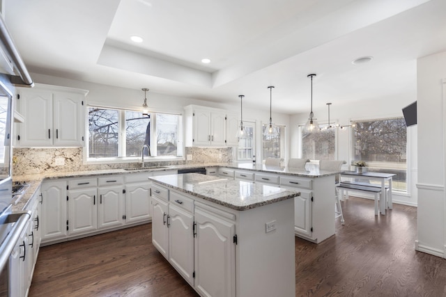 kitchen featuring dark wood-style floors, a tray ceiling, a center island, a sink, and a peninsula