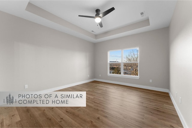 spare room featuring a raised ceiling, visible vents, ceiling fan, wood finished floors, and baseboards