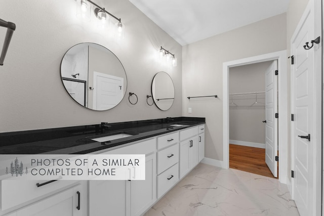 full bathroom with double vanity, marble finish floor, baseboards, and a sink