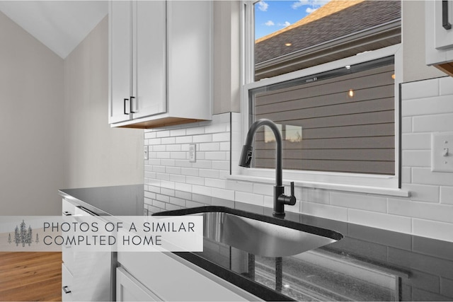 kitchen featuring tasteful backsplash, dark countertops, white cabinetry, and a sink