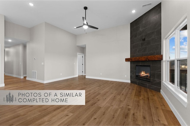 unfurnished living room with a tile fireplace, visible vents, baseboards, and wood finished floors