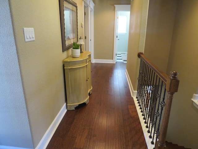 hall featuring baseboards, dark wood-style flooring, and an upstairs landing