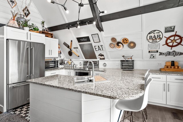 kitchen featuring a sink, white cabinetry, appliances with stainless steel finishes, light stone countertops, and a kitchen bar