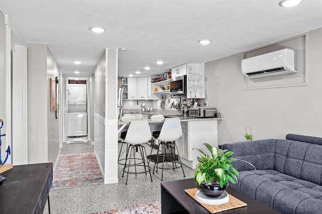 living room with light speckled floor, recessed lighting, an AC wall unit, indoor wet bar, and stacked washer and clothes dryer