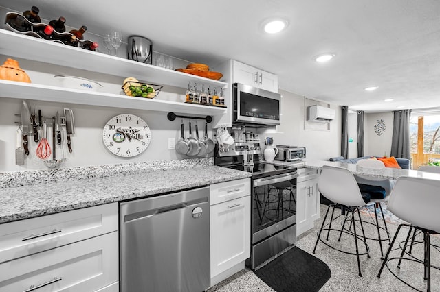 kitchen with recessed lighting, white cabinetry, an AC wall unit, appliances with stainless steel finishes, and light stone countertops