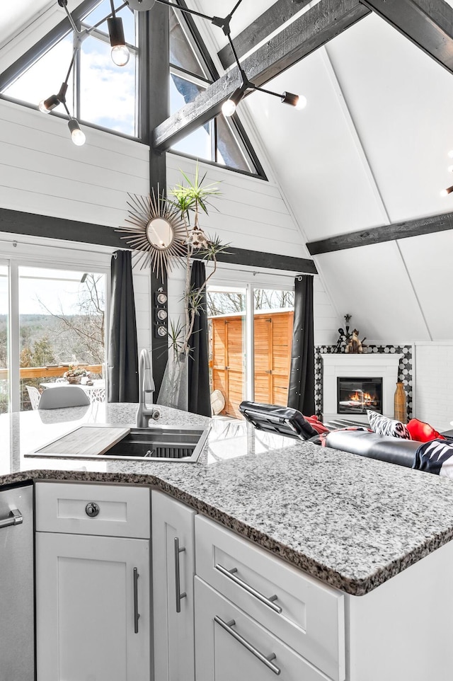 kitchen with a wealth of natural light, white cabinetry, a sink, and a glass covered fireplace