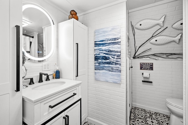 bathroom featuring toilet, ornamental molding, vanity, brick wall, and tile patterned flooring