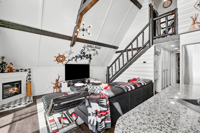 living room with high vaulted ceiling, a glass covered fireplace, stairs, and wood finished floors