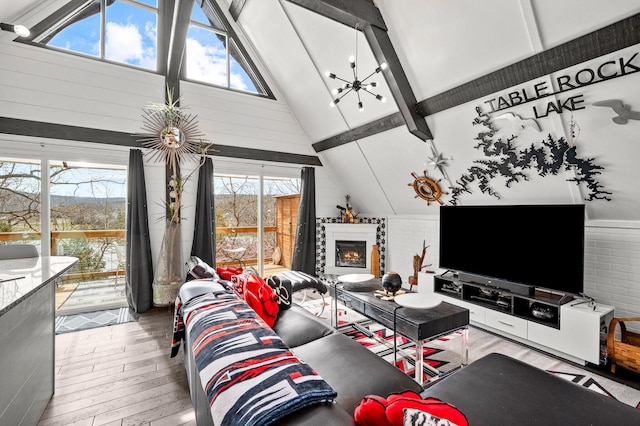 living room with a notable chandelier, a glass covered fireplace, wood finished floors, high vaulted ceiling, and beamed ceiling