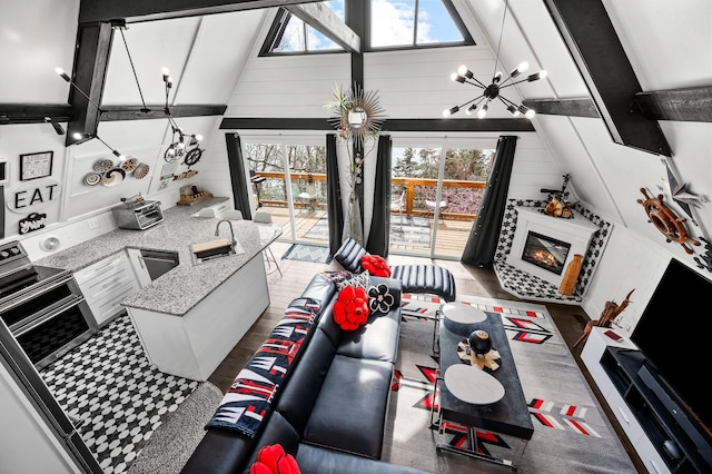 living room featuring an inviting chandelier, a glass covered fireplace, wooden walls, wood finished floors, and high vaulted ceiling