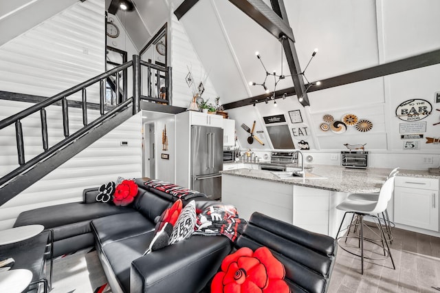 living area featuring beam ceiling, a toaster, light wood-style flooring, high vaulted ceiling, and stairs