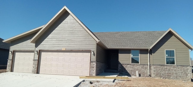 view of front of property featuring an attached garage, stone siding, driveway, and roof with shingles