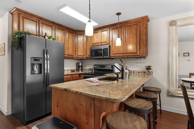 kitchen with a peninsula, appliances with stainless steel finishes, brown cabinetry, and a sink