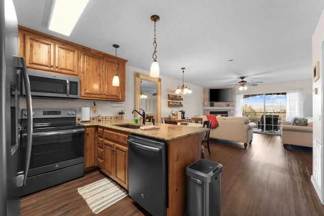 kitchen featuring stainless steel appliances, a peninsula, a sink, open floor plan, and brown cabinetry