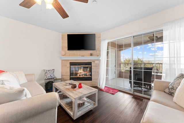 living area with a large fireplace, ceiling fan, visible vents, and wood finished floors