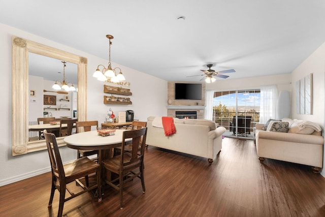 dining area with dark wood-type flooring, a fireplace, baseboards, and ceiling fan with notable chandelier