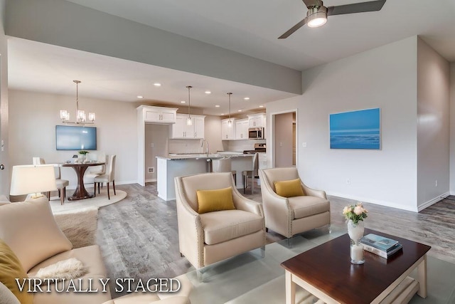 living room featuring light wood-style floors, recessed lighting, baseboards, and ceiling fan with notable chandelier