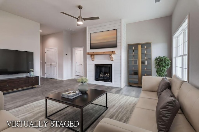 living area with a fireplace, visible vents, ceiling fan, wood finished floors, and baseboards