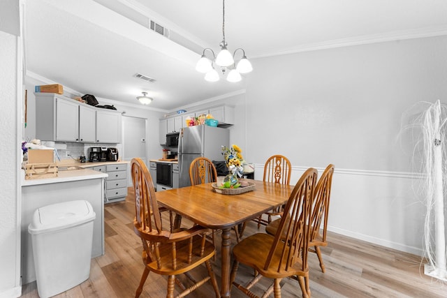 dining area with an inviting chandelier, light wood-type flooring, visible vents, and crown molding