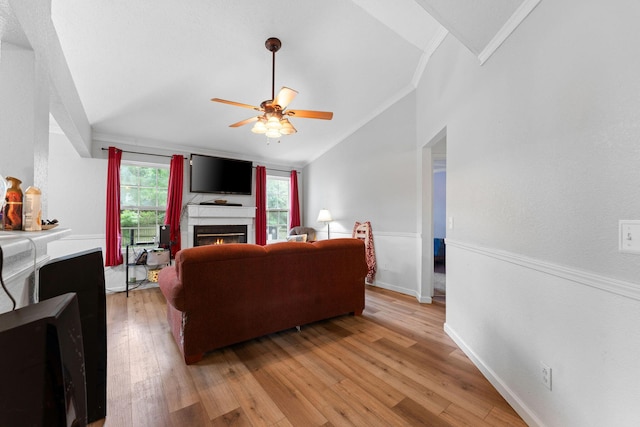 living area featuring light wood-style flooring, a ceiling fan, vaulted ceiling, a lit fireplace, and ornamental molding