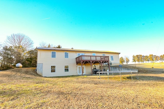 rear view of house featuring a trampoline, a lawn, and a deck