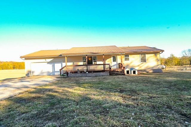 view of front of home with covered porch, a front yard, metal roof, a garage, and driveway