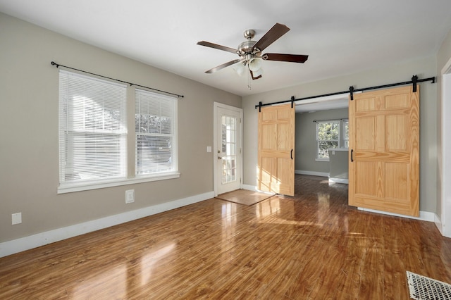 interior space with a barn door, baseboards, visible vents, ceiling fan, and wood finished floors