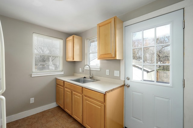 kitchen featuring light tile patterned floors, light countertops, light brown cabinets, a sink, and baseboards