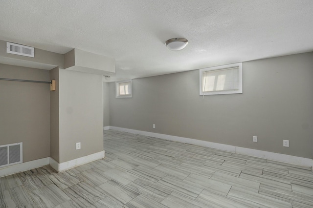 below grade area with visible vents, a textured ceiling, and baseboards