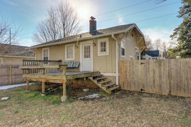 rear view of property featuring a shingled roof, a chimney, fence, and a wooden deck